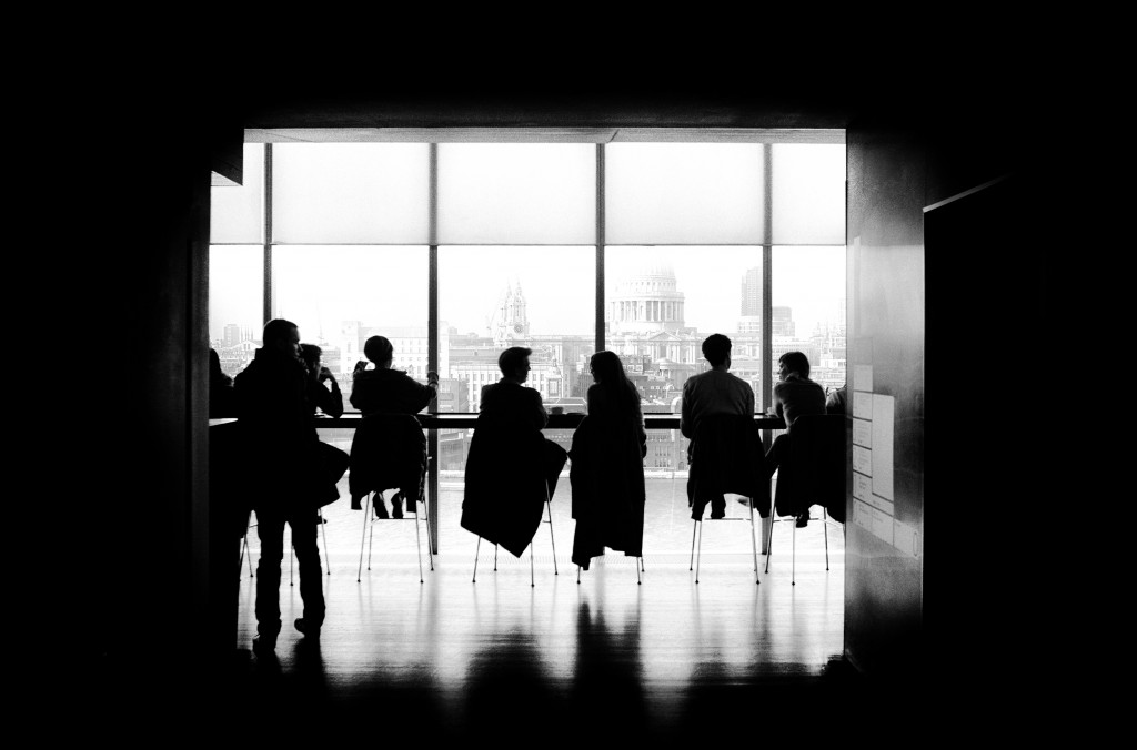 Black and white photo of a boardroom with silhouettes of people seated near a large window, creating dramatic shadows."